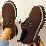 Brown suede shoes with black soles held by a person against a neutral background