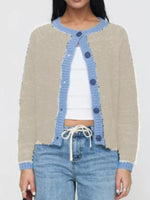 Person wearing a beige cardigan with blue trim, white top, and blue jeans on a plain background