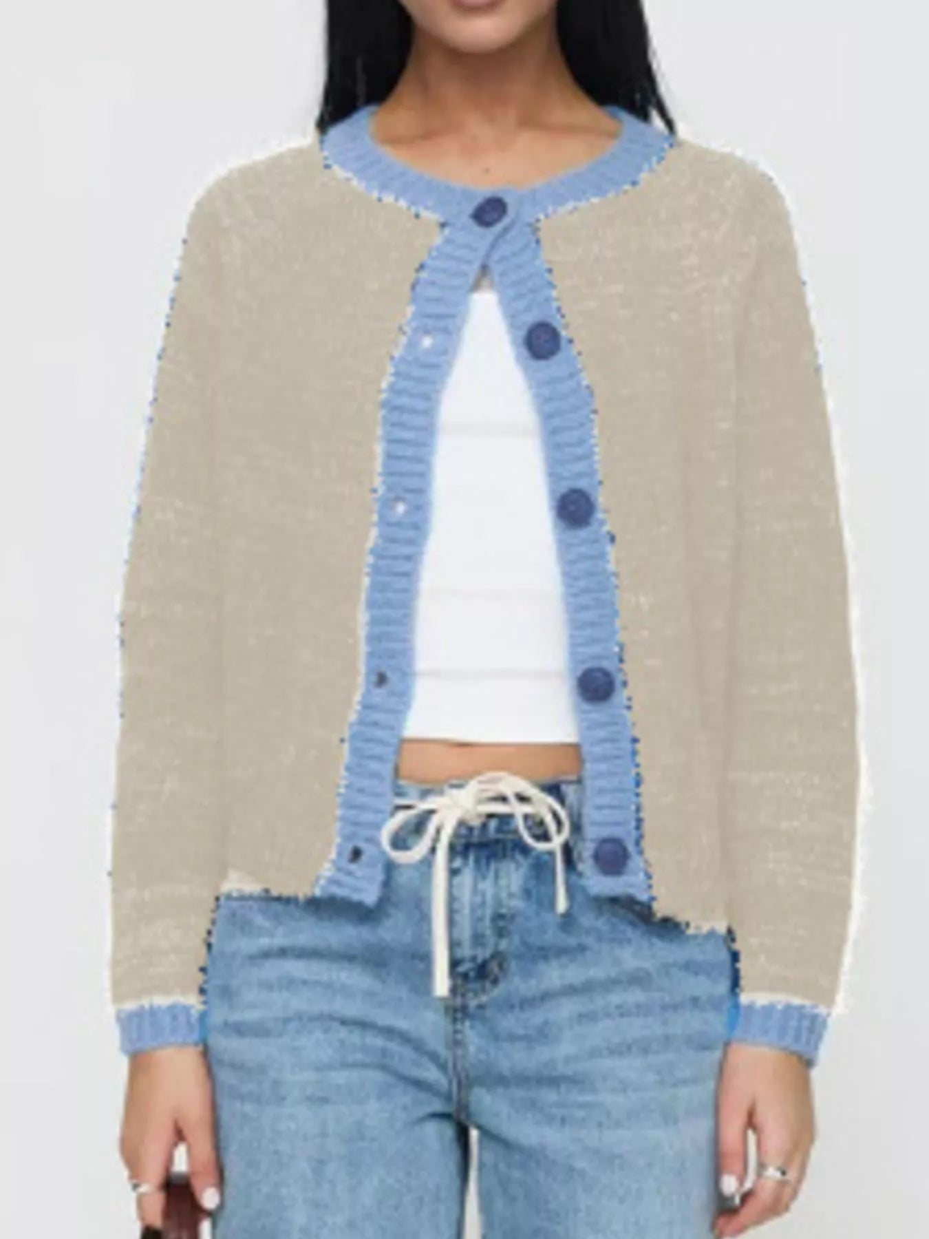 Person wearing a beige cardigan with blue trim, white top, and blue jeans on a plain background