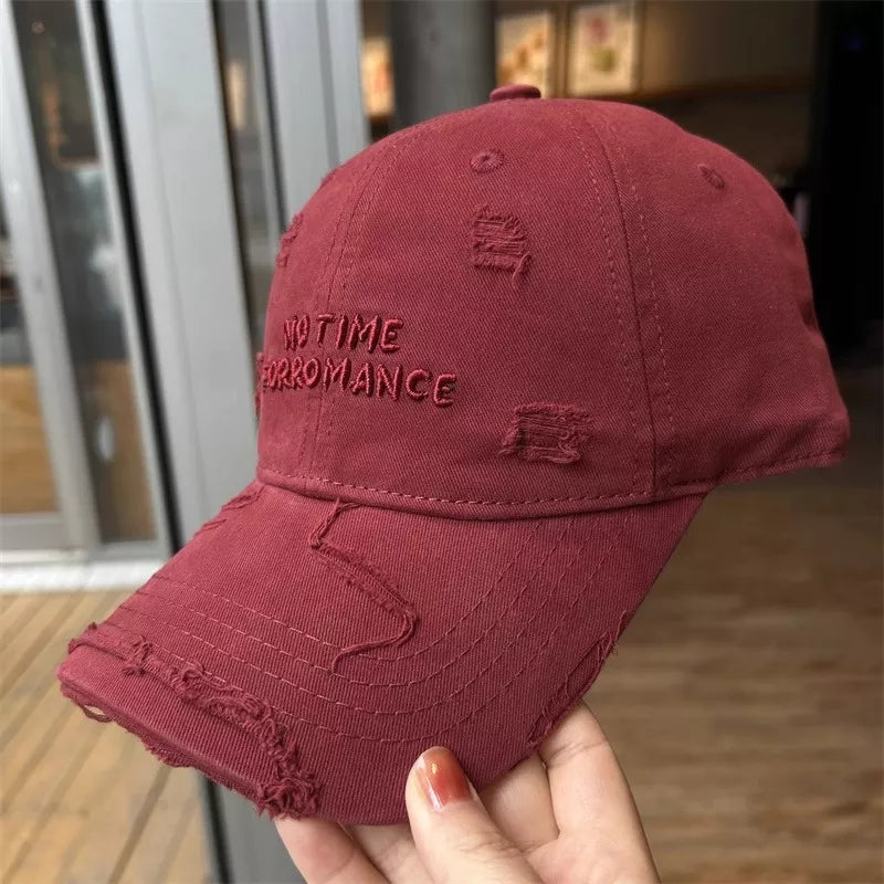 Red cap with 'No Time For Romance' text held by a hand against a blurred indoor background
