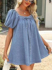 Woman wearing a blue denim dress with puff sleeves outdoors.
