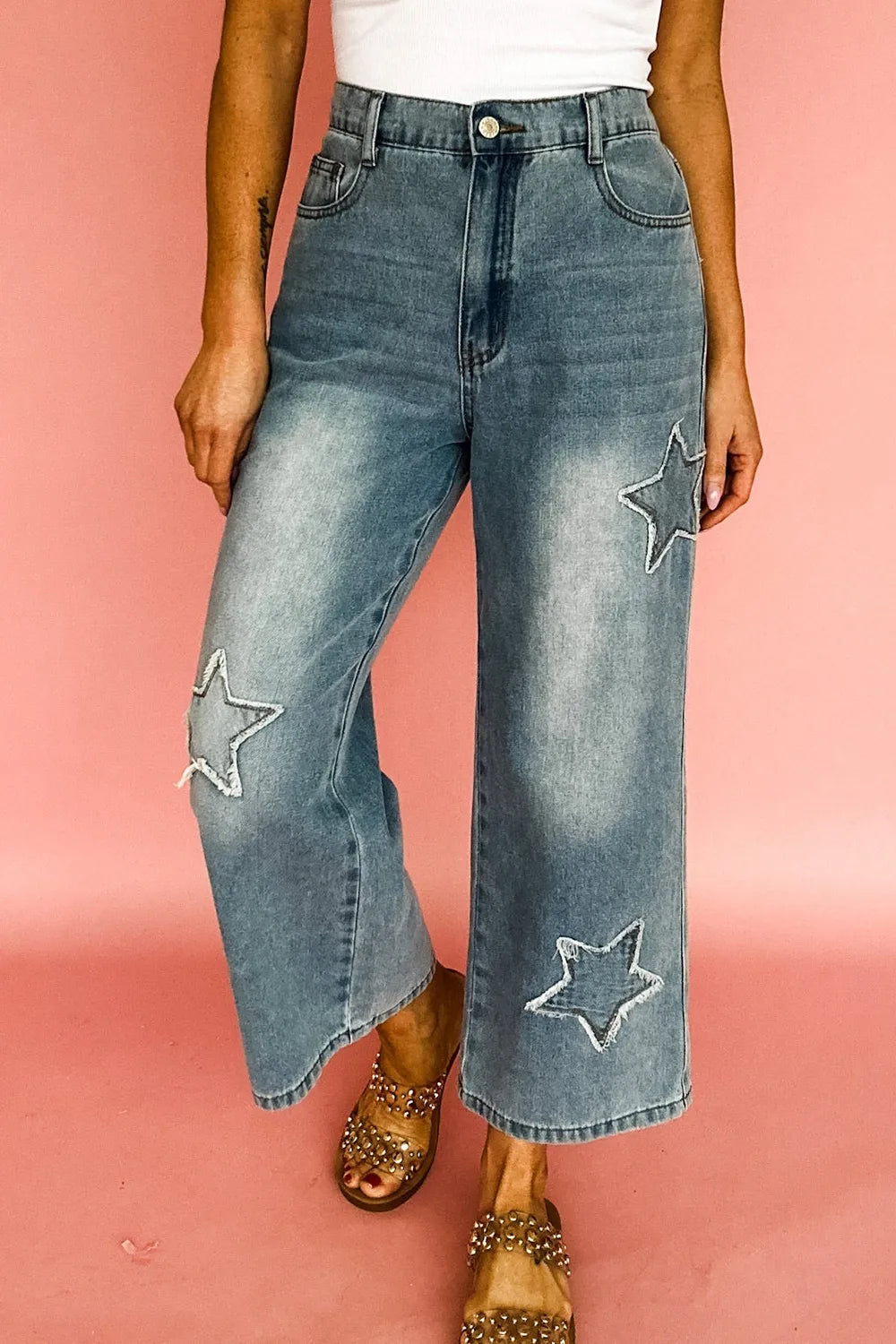Person wearing blue jeans with star patches on a pink background