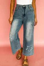 Person wearing blue jeans with star patches on a pink background