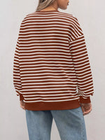 Person wearing a brown and white striped sweater with light blue jeans against a plain background