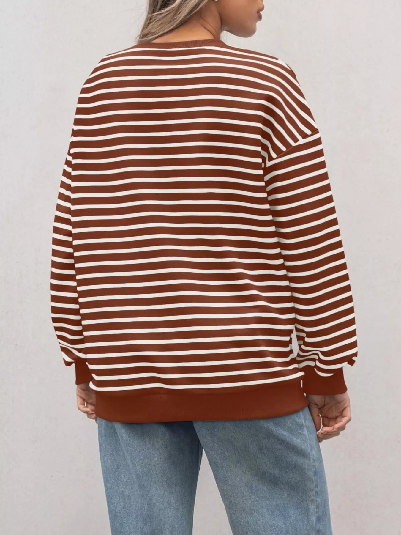 Person wearing a brown and white striped sweater with light blue jeans against a plain background