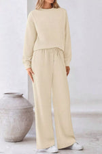 Woman wearing a beige outfit standing next to a textured vase on a light background