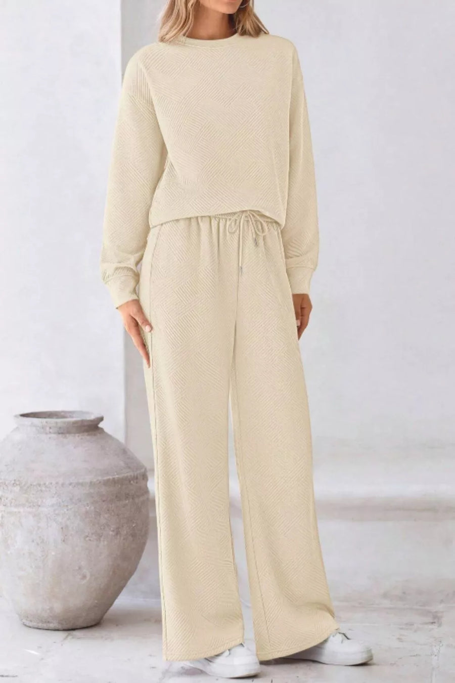 Woman wearing a beige outfit standing next to a textured vase on a light background