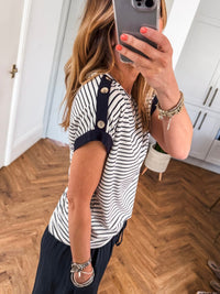 Person taking a mirror selfie wearing a striped shirt with buttons and dark pants.