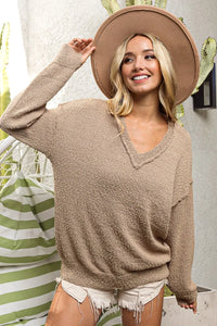 Woman wearing a beige sweater and hat, standing in a casual setting with plants.