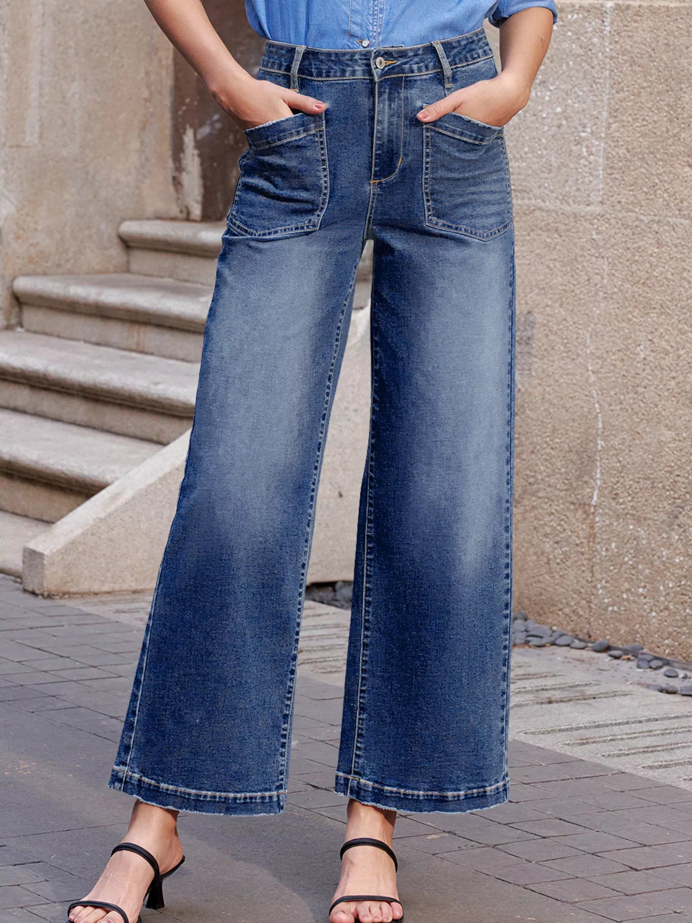 Person wearing blue wide-leg jeans standing on a stone pavement.
