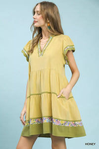 Woman wearing a yellow dress with floral trim on a light blue background