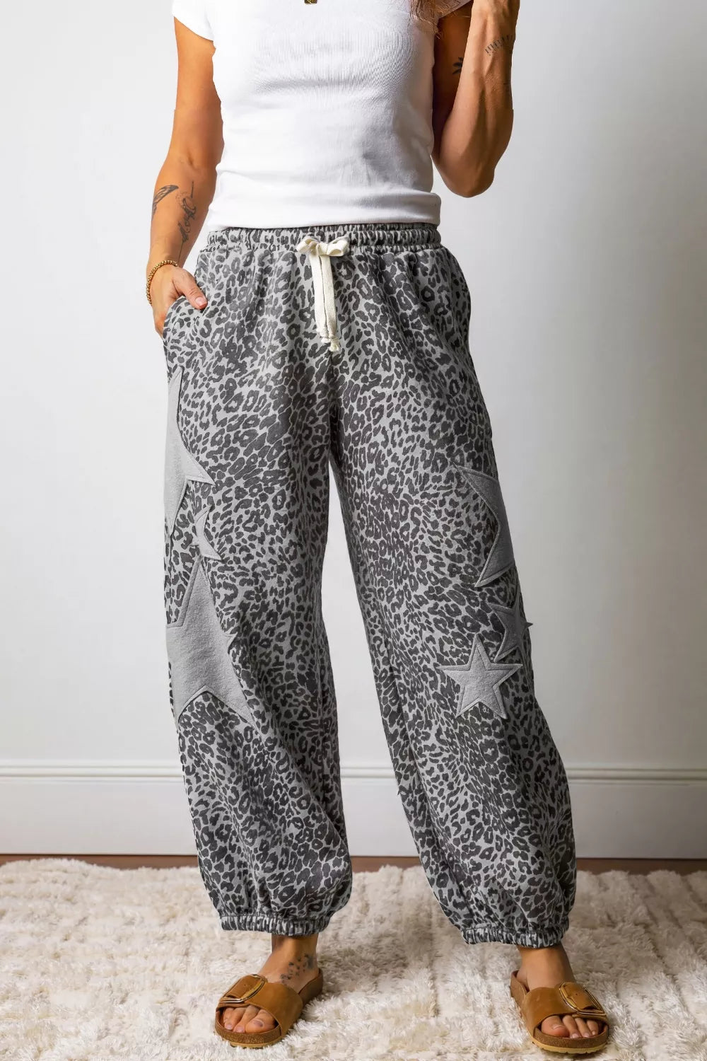 Person wearing gray leopard print pants with a white top against a plain background