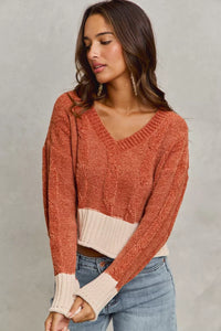 Woman wearing a rust-colored sweater with a white trim against a gray background