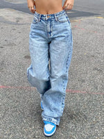 Person wearing high-waisted blue jeans and blue sneakers on a street.