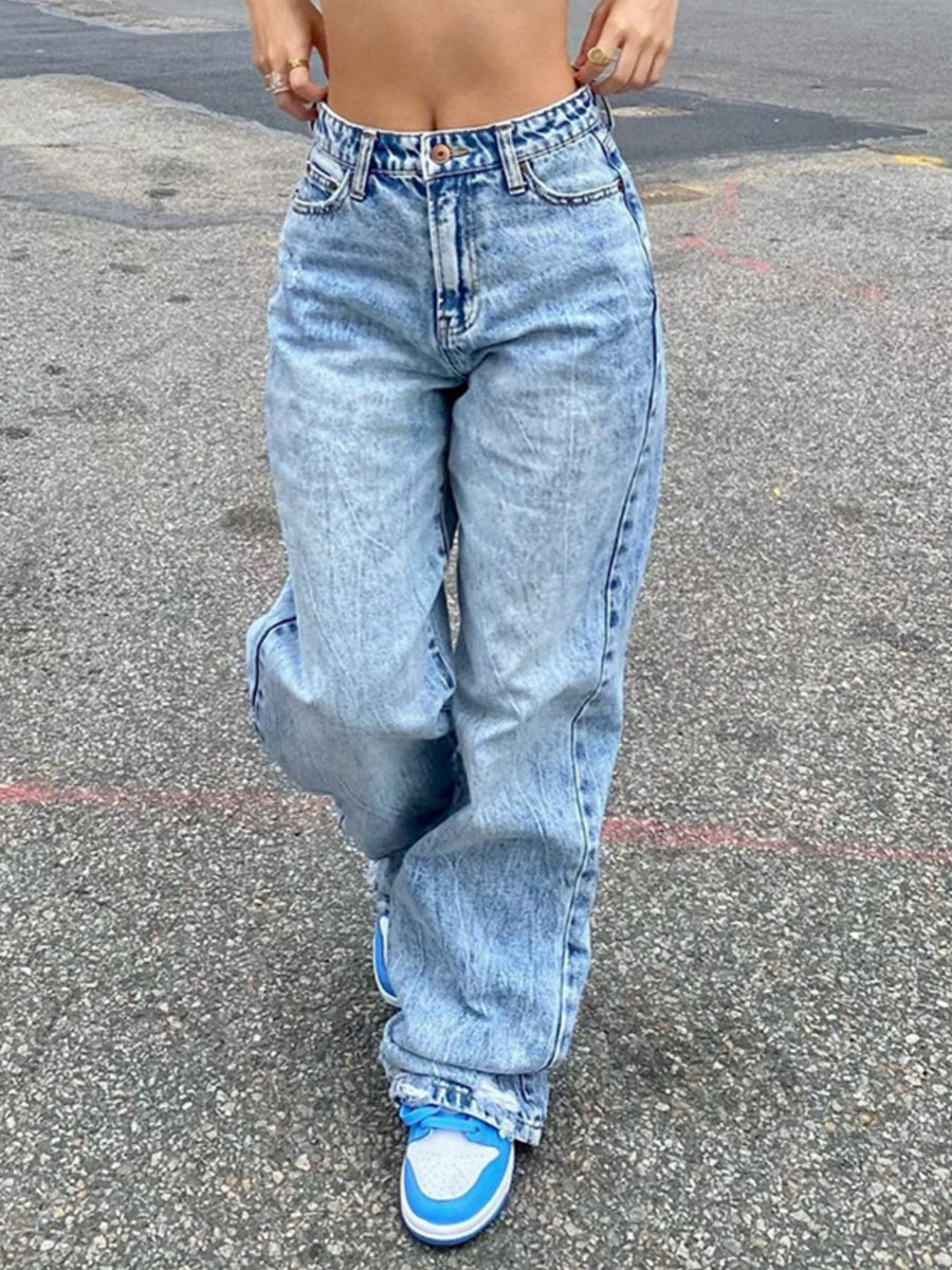 Person wearing high-waisted blue jeans and blue sneakers on a street.
