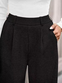 Black pleated pants worn by a person on a light gray background