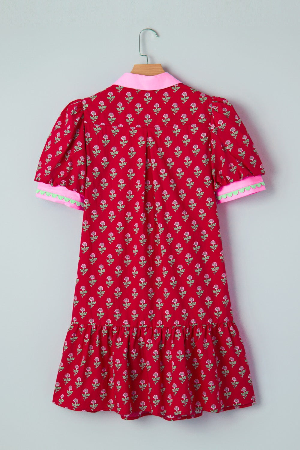 Red floral dress with pink trim on a hanger against a gray background