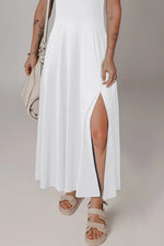 Person wearing a white dress with a slit, holding a beige handbag on a plain background