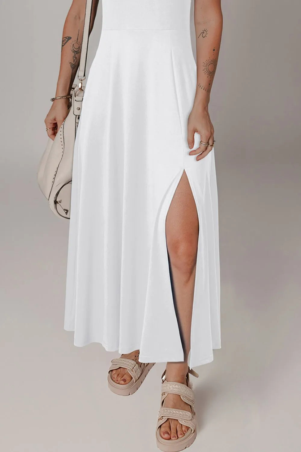Person wearing a white dress with a slit, holding a beige handbag on a plain background