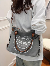 Person holding a gray bag with 'Paris' text in a room.