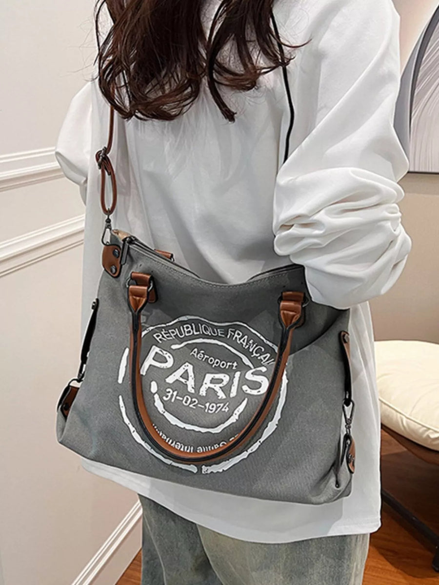 Person holding a gray bag with 'Paris' text in a room.