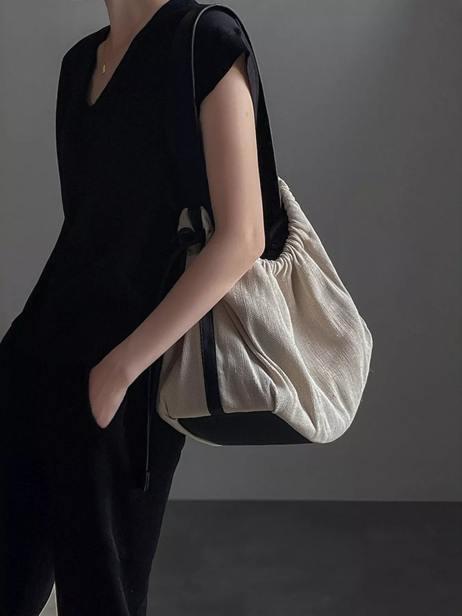 Person wearing a black outfit holding a beige bag against a gray background