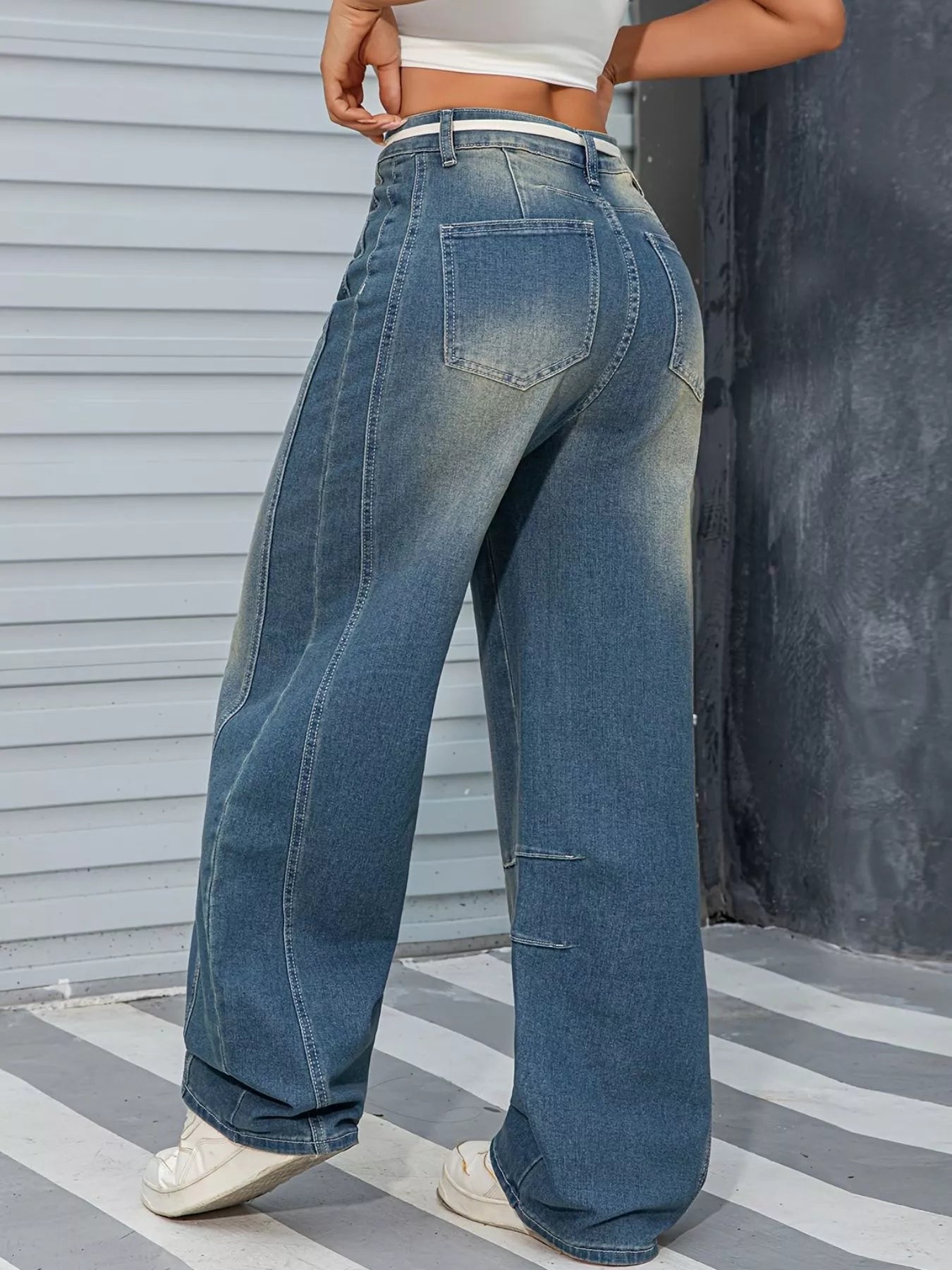 Person wearing wide-leg jeans standing against a striped floor and gray wall.