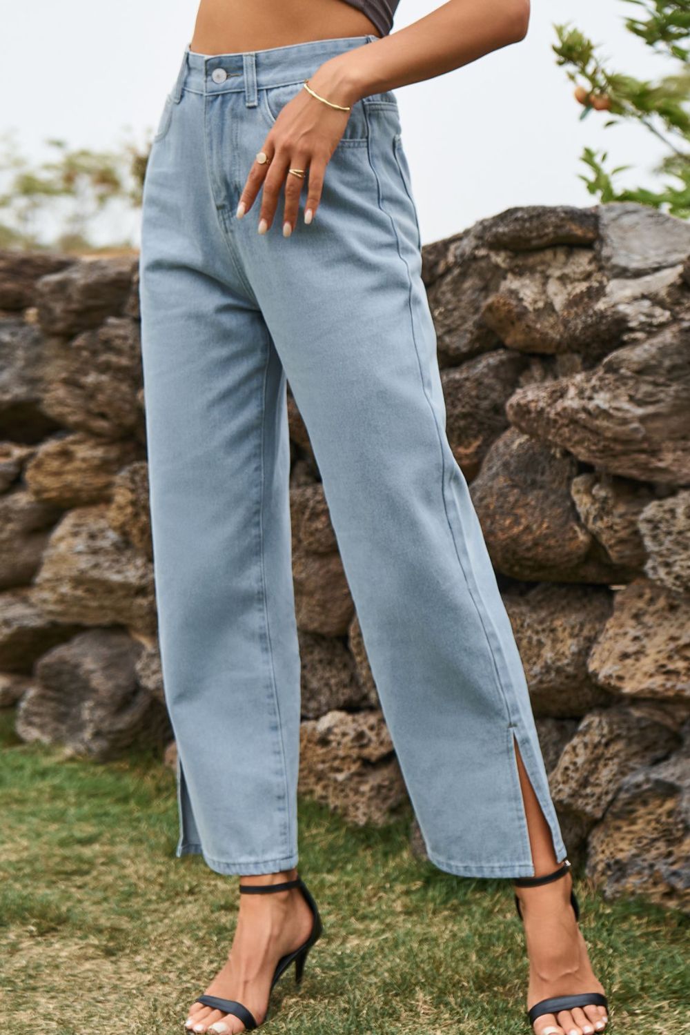 Person wearing light blue jeans with a stone wall and grass background