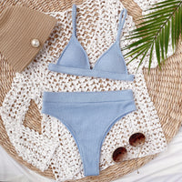 Blue bikini set on a textured surface with a handbag and sunglasses