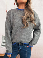 Person wearing a gray sweater with blue trim and blue jeans against a neutral background