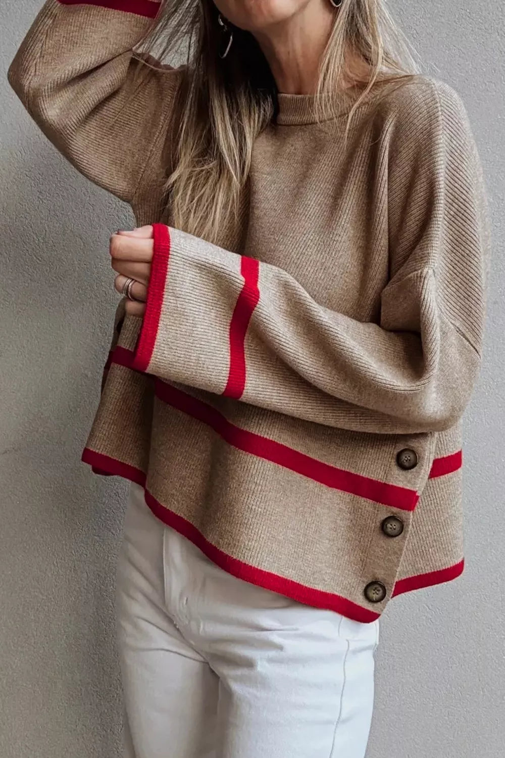 Beige sweater with red trim worn by a person against a neutral background