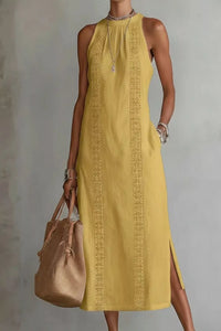 Woman wearing a yellow dress with intricate patterns, holding a brown bag against a plain background