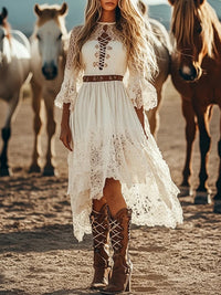 Woman in a white lace dress and brown boots standing in front of horses.