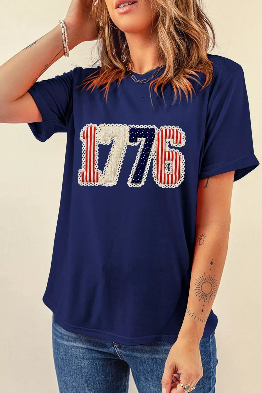 Navy blue t-shirt with '1776' design worn by a person on a beige background