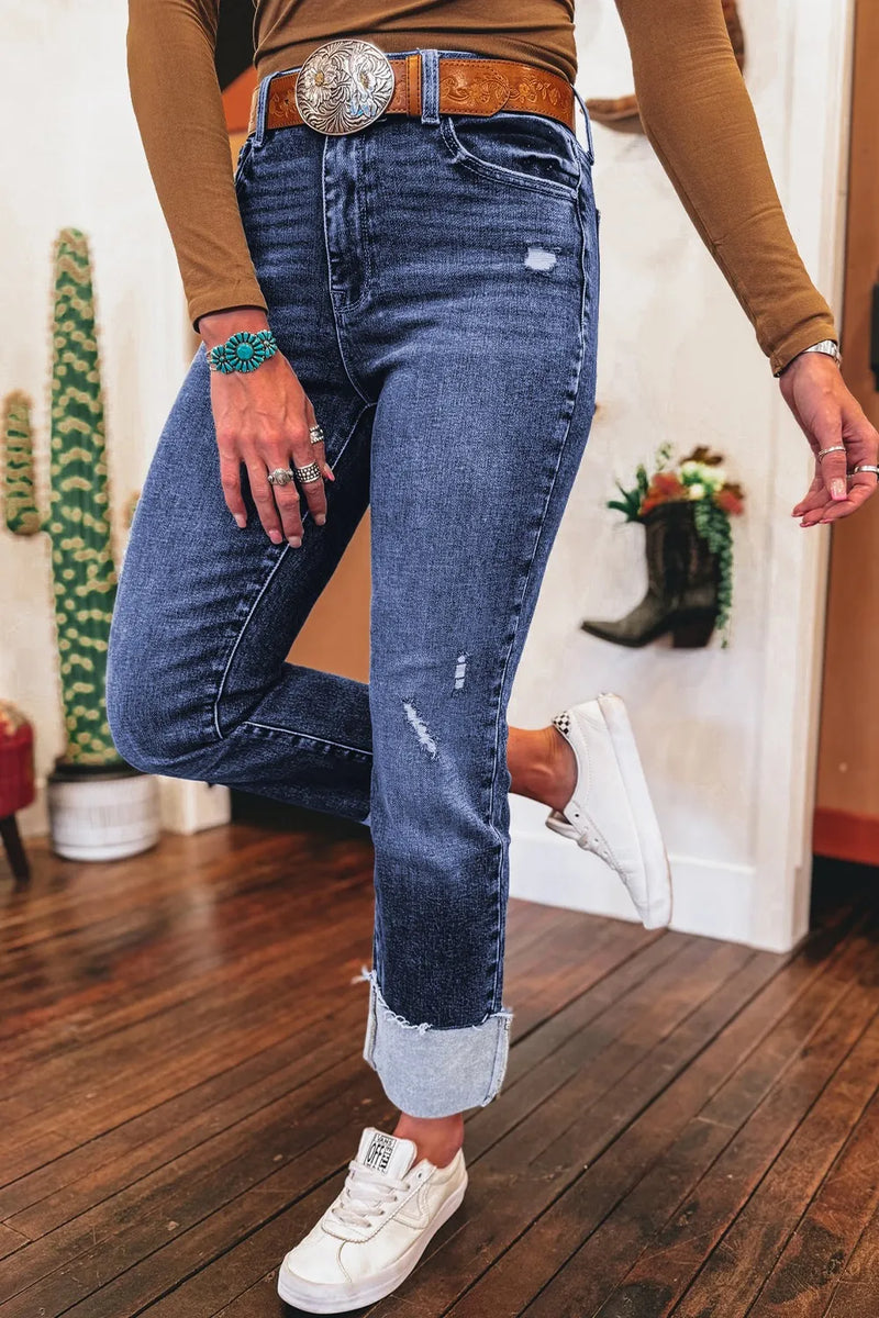Person wearing blue jeans and a brown top with a belt, standing on a wooden floor.