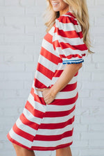 Woman wearing a red and white striped dress against a white brick wall.