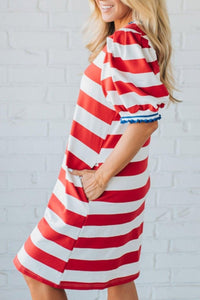 Woman wearing a red and white striped dress against a white brick wall.