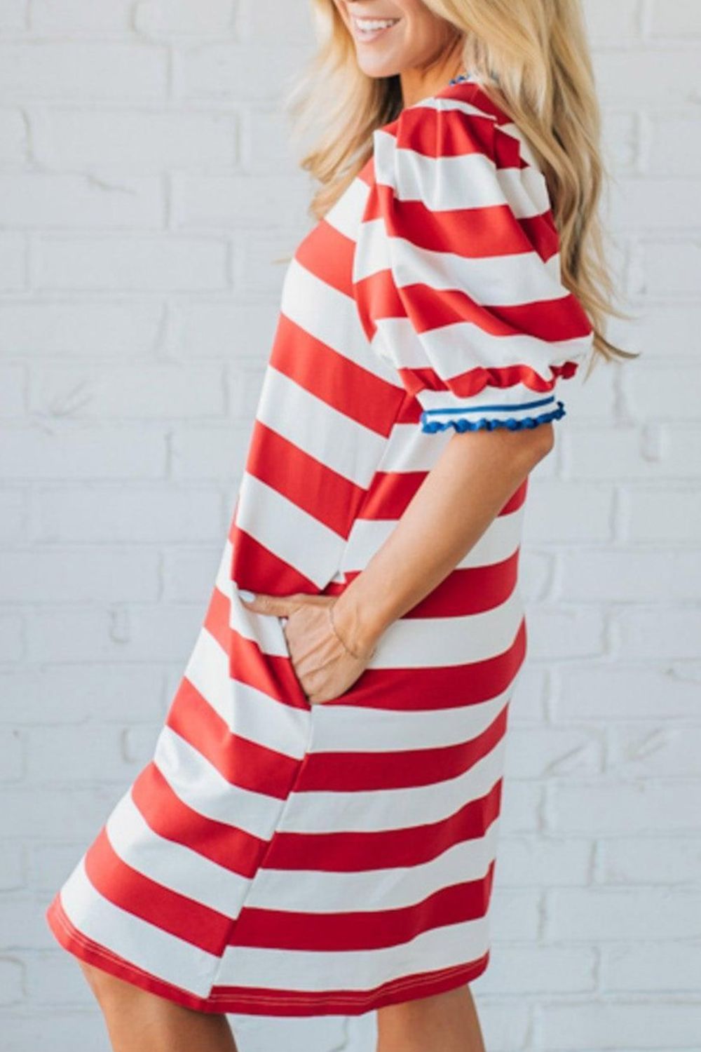 Woman wearing a red and white striped dress against a white brick wall.