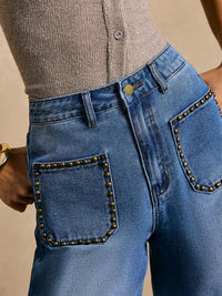 Blue jeans with studded details worn by a person on a beige background