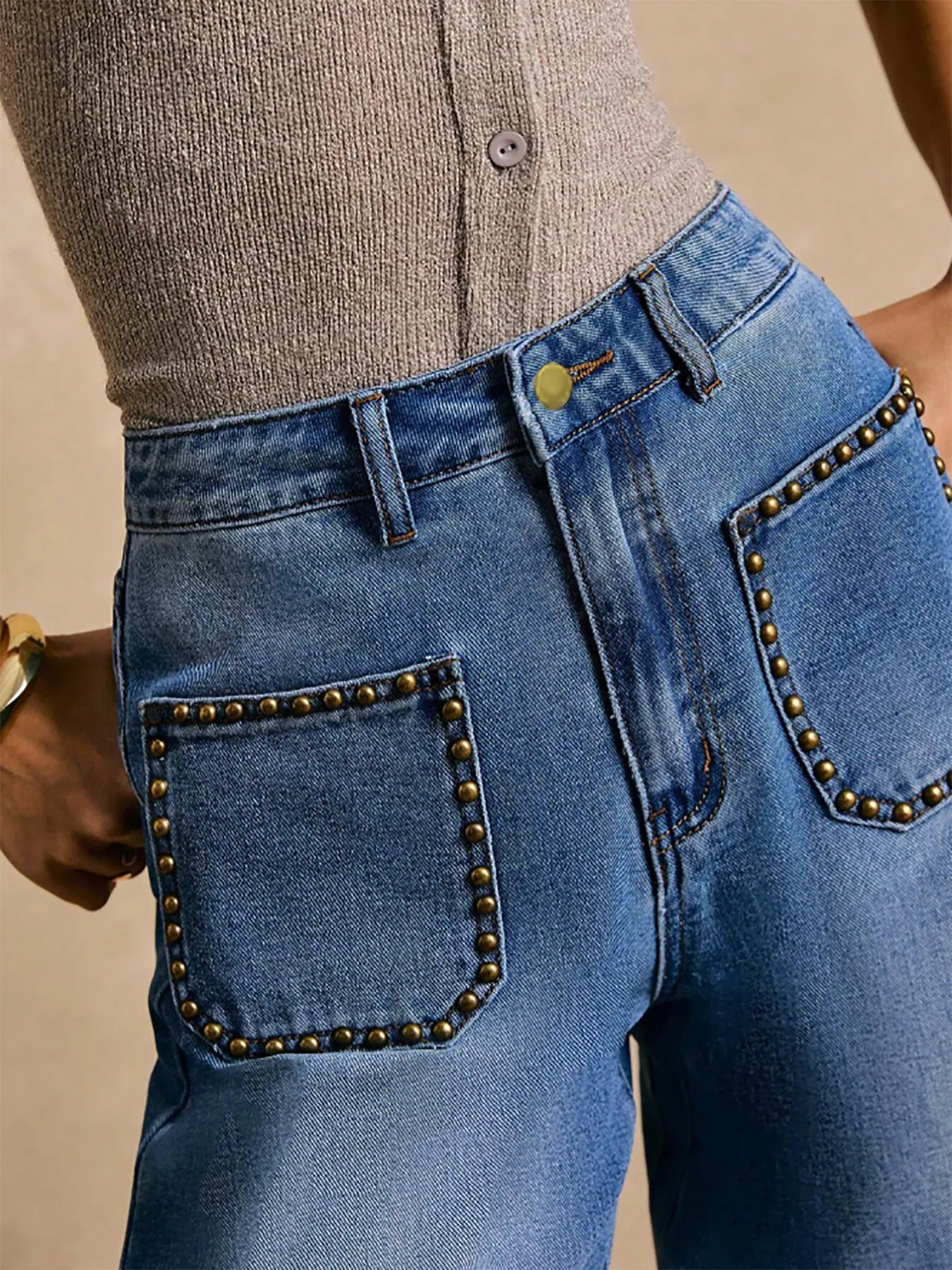 Blue jeans with studded details worn by a person on a beige background