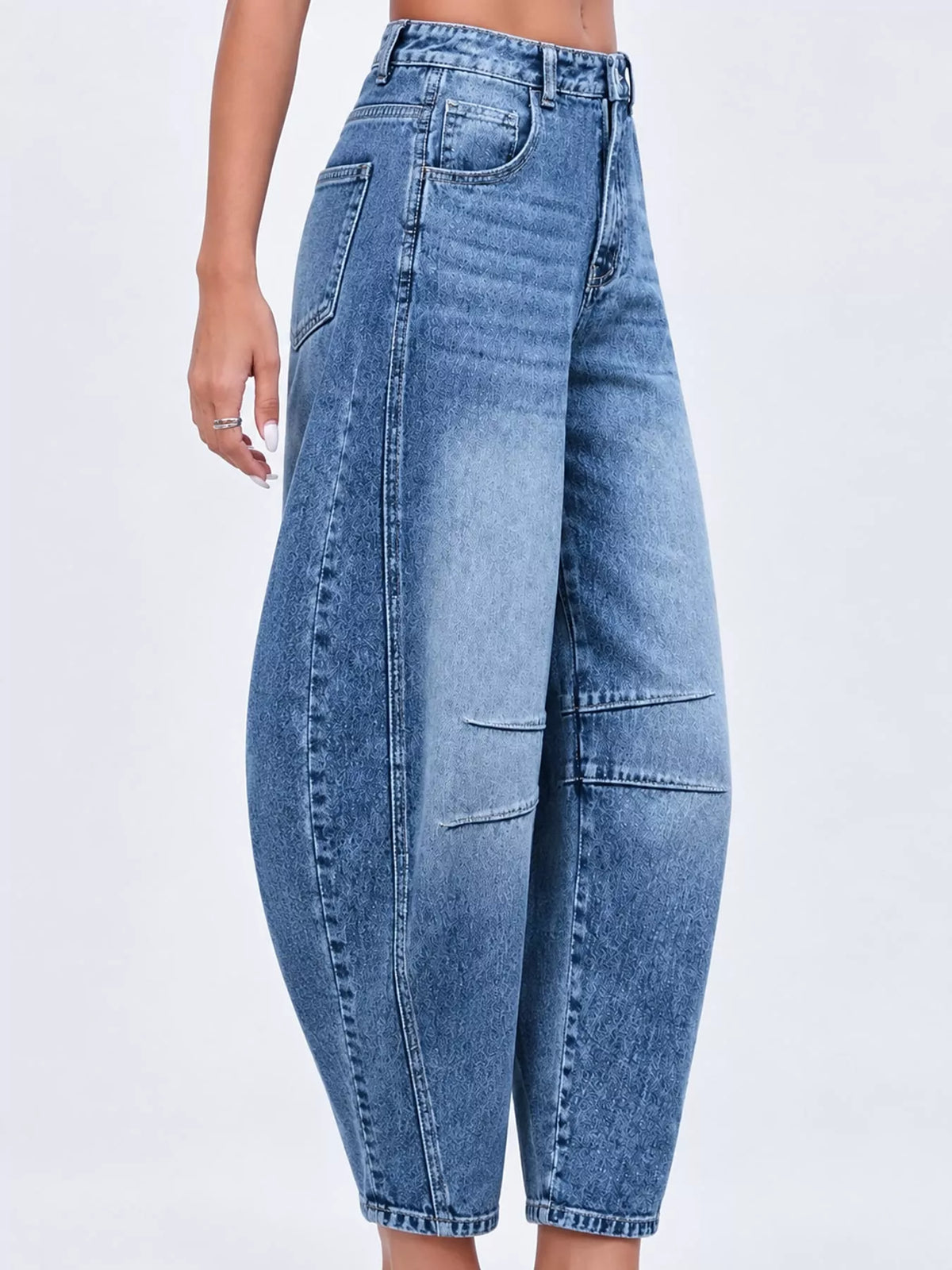 A model wearing high-waisted, wide-leg cropped blue denim jeans with diagonal seam details and distressed patches on the front, shown against a plain white background.