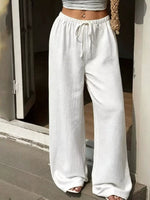 Person wearing white wide-leg pants and a gray top, standing on a stone floor.