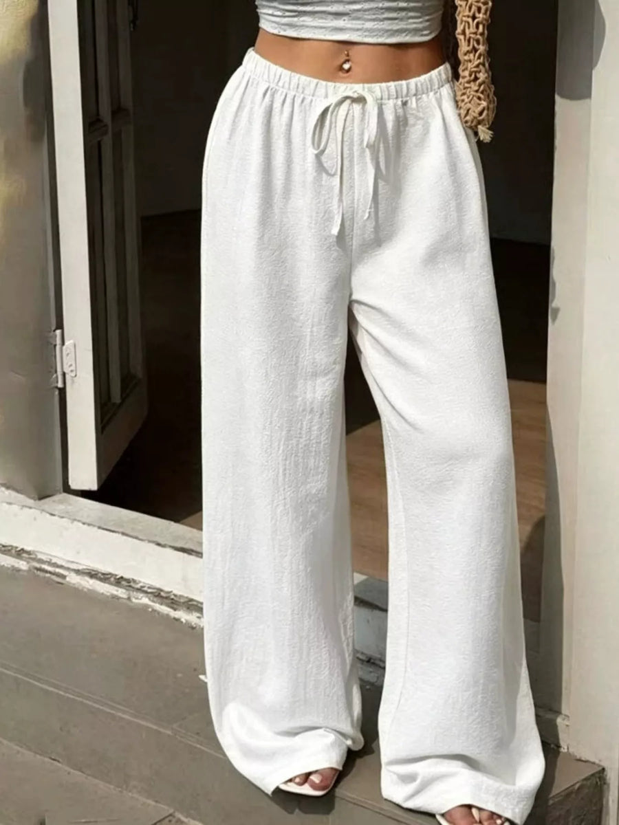 Person wearing white wide-leg pants and a gray top, standing on a stone floor.