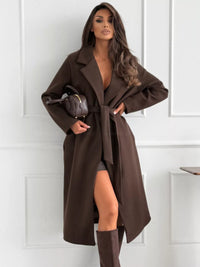 Woman wearing a brown coat with a white paneled wall background