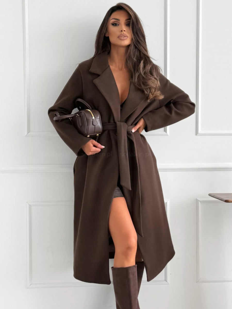 Woman wearing a brown coat with a white paneled wall background