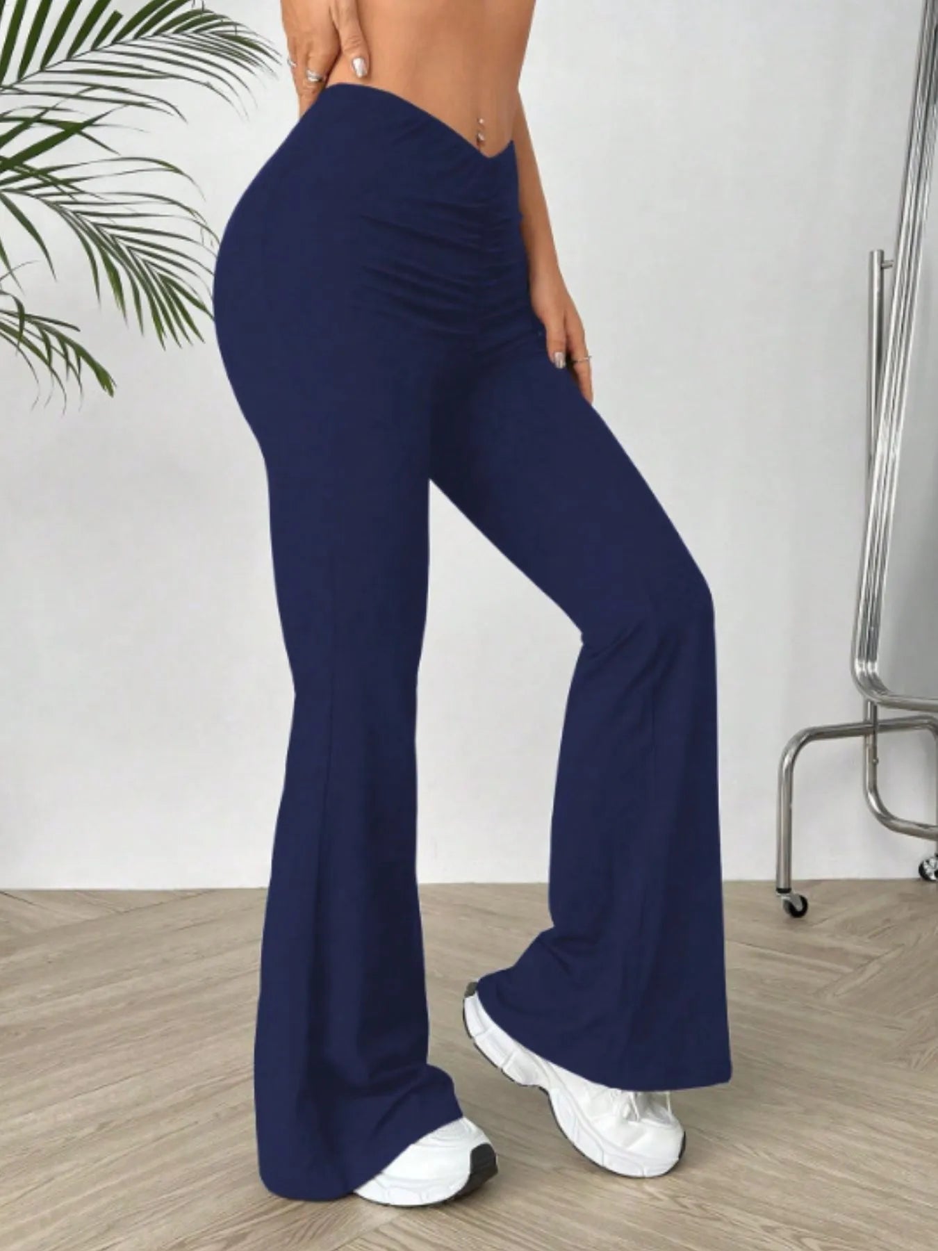 Navy blue flared pants worn by a person on a wooden floor with a white wall background.