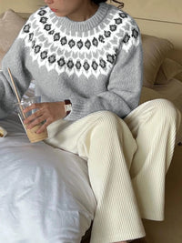 Person wearing a gray sweater with a floral pattern and white pants, sitting on a couch.