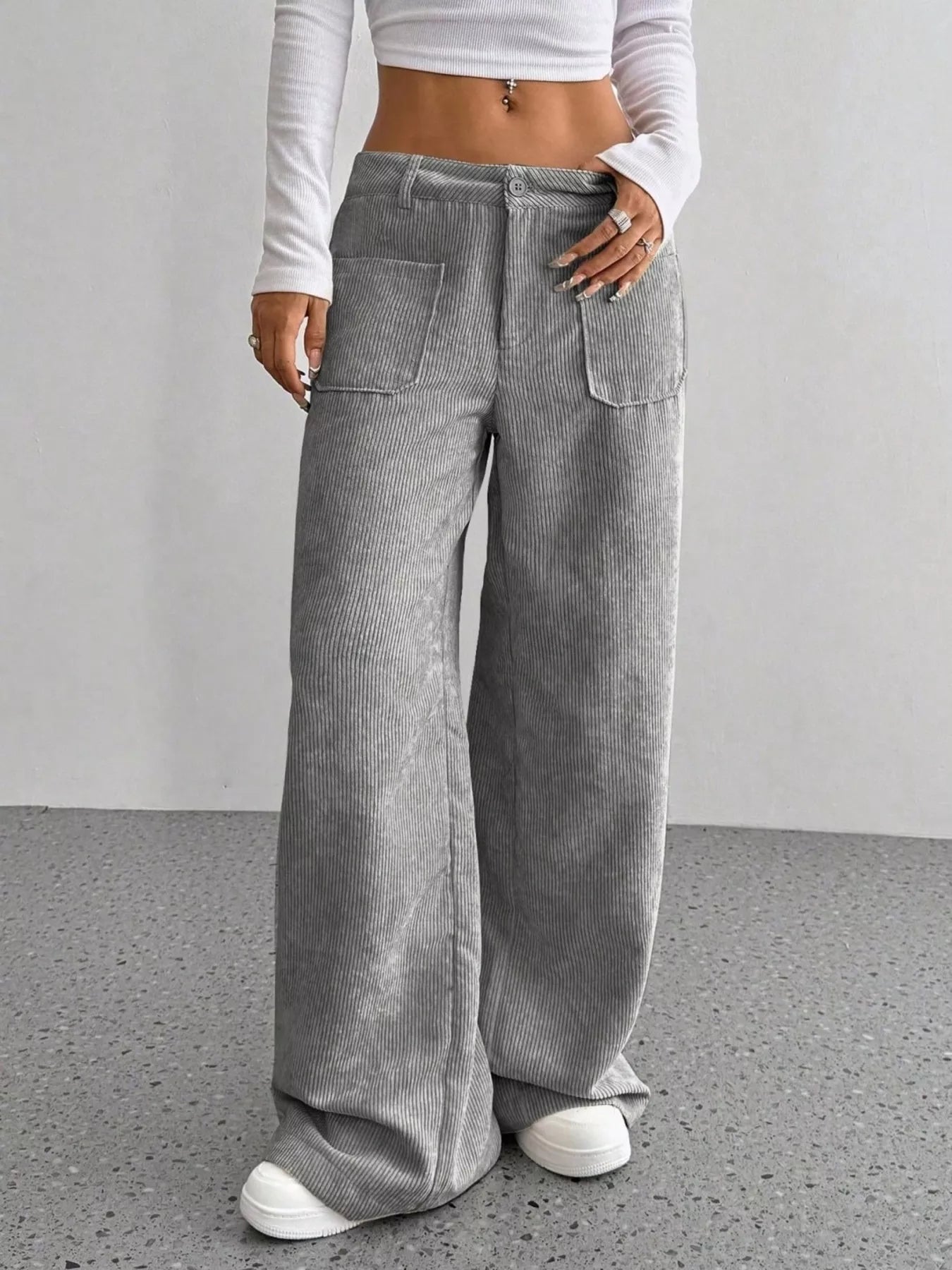 Person wearing gray wide-leg pants and a white cropped top on a plain background