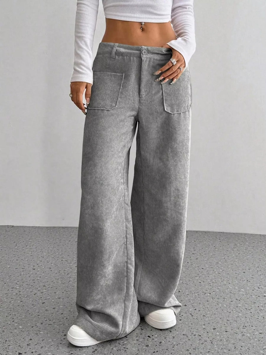 Person wearing gray wide-leg pants and a white cropped top on a plain background