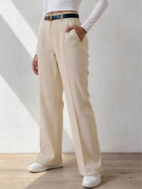 Person wearing beige wide-leg pants with a white top and white shoes on a light wooden floor.